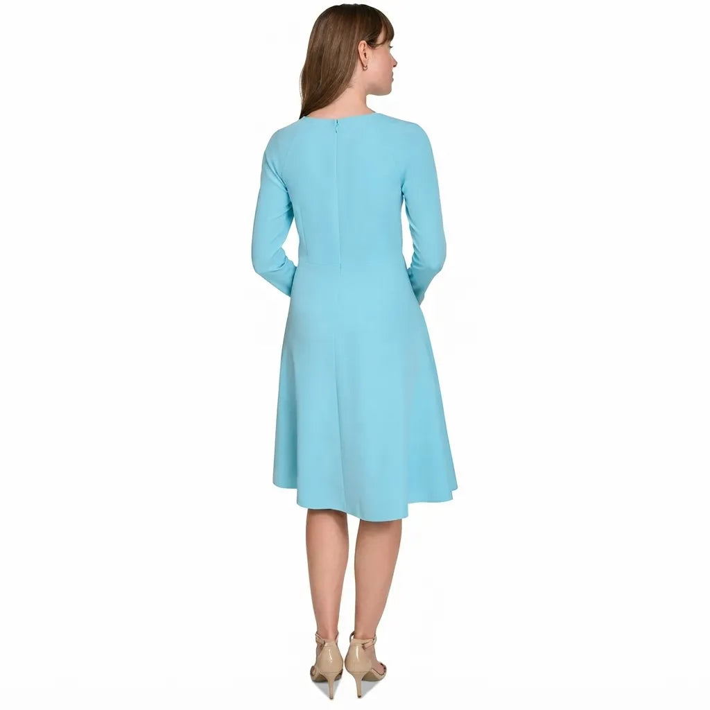 A woman shown from the back wearing a light blue long-sleeve knee-length dress, paired with beige high heels, against a plain white background.