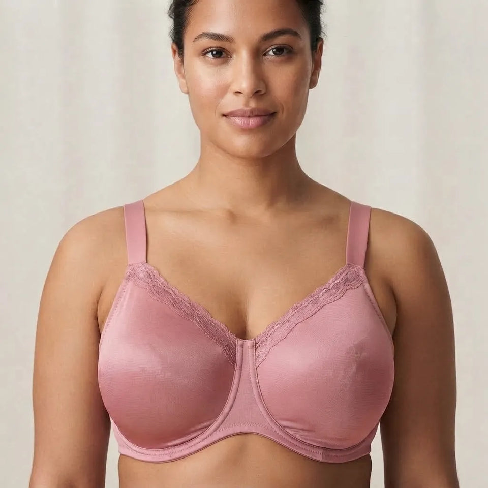 A woman wearing a dusty pink wireless bra with lace-trimmed cups and wide shoulder straps, shown from the chest up against a soft beige background.