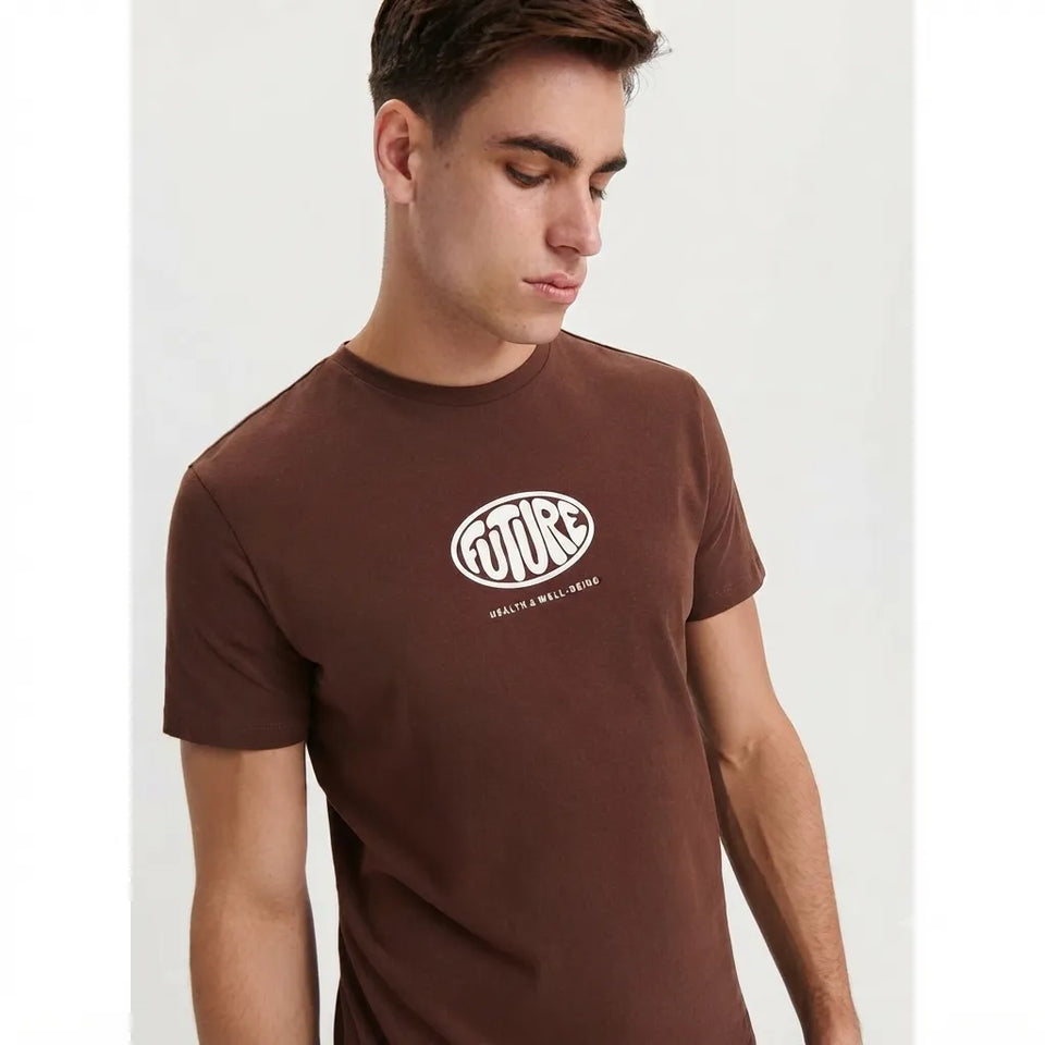 A man wearing a brown crewneck t-shirt with a white 'FUTURE' graphic logo on the chest, photographed against a light gray background.