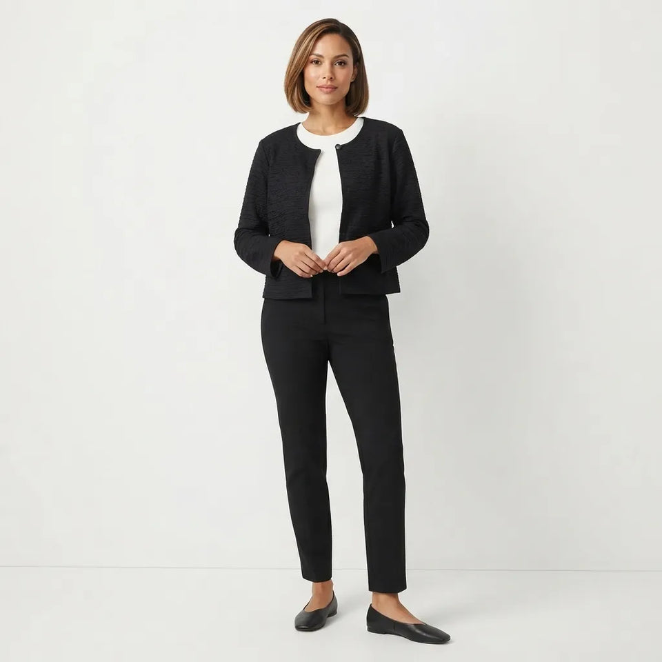 A woman modeling a black textured cropped jacket with a white collar, paired with black trousers and black flats, against a clean white studio background.