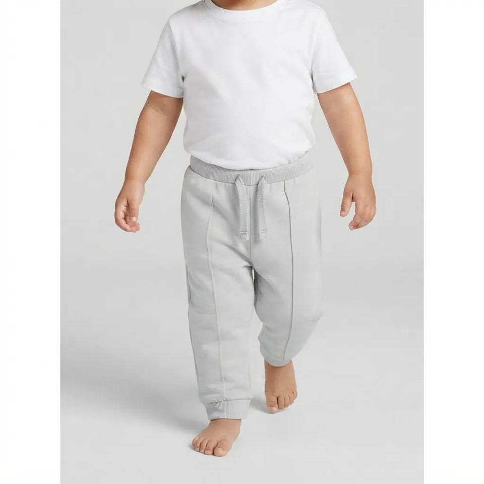 A toddler walking barefoot wearing a plain white short-sleeve t-shirt and light gray sweatpants against a light gray studio background.