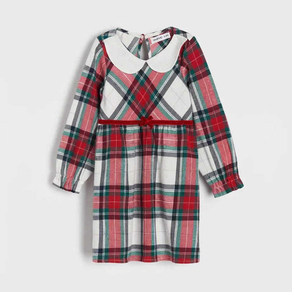 A long-sleeve children's dress with a red, green, and white tartan plaid pattern, featuring a solid white Peter Pan collar and a matching red waist tie, shown against a light gray background.