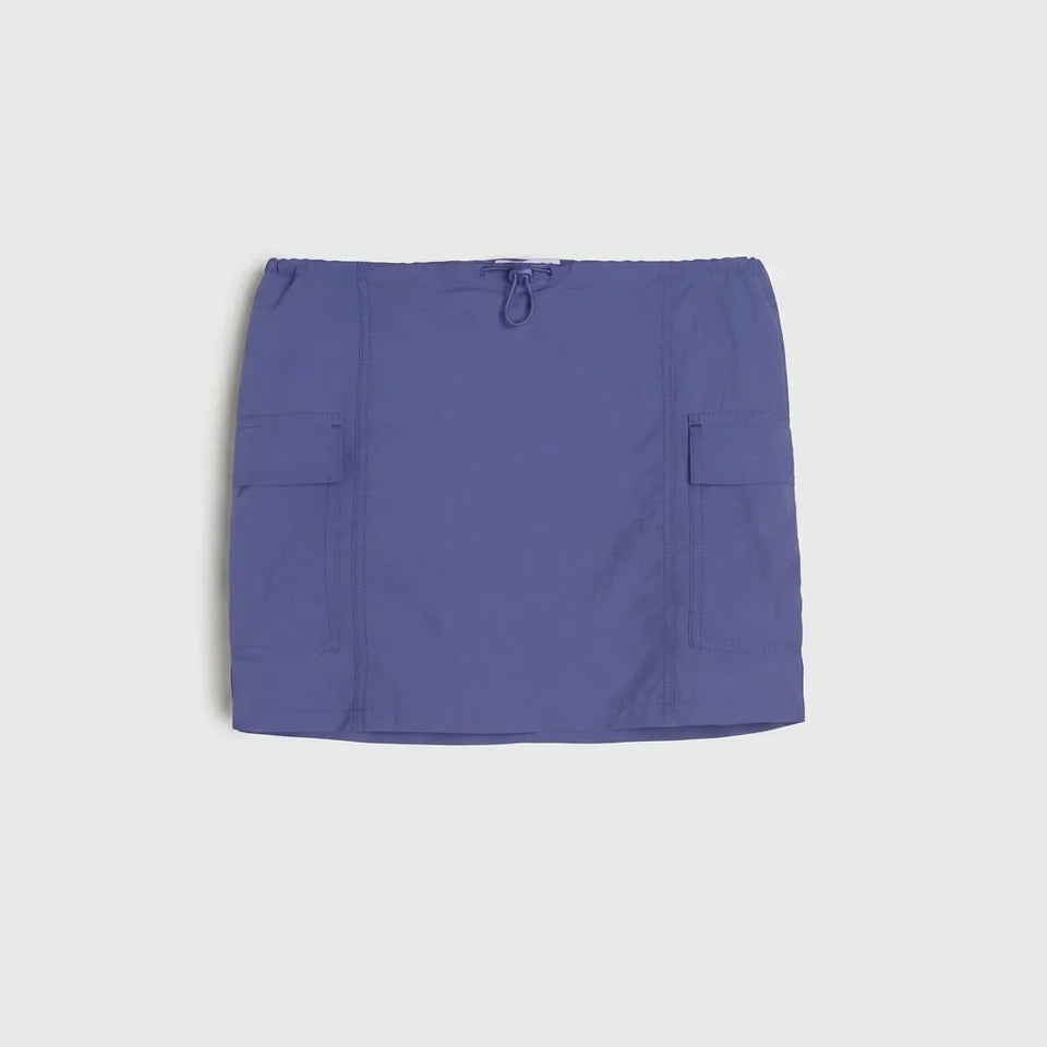 A slate blue utility mini skirt with side pockets and a drawstring waist, laid flat against a light gray background.