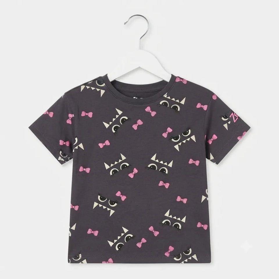 A kids' short-sleeve t-shirt in dark gray, featuring an all-over print of cartoon monsters with pink bows, black eyes, and white fangs, hanging on a white plastic hanger against a light gray background.