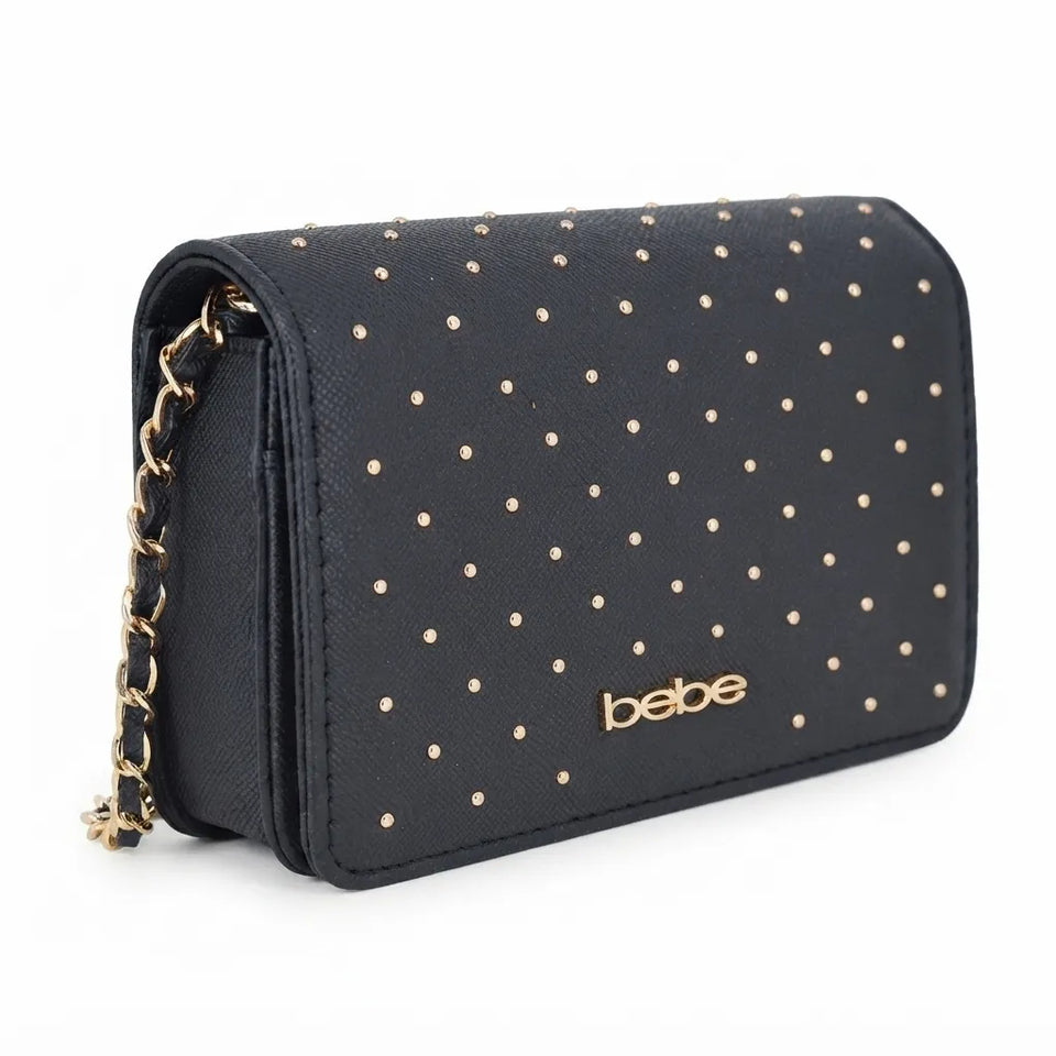 A black textured shoulder bag with gold studs in a polka dot pattern, featuring a gold chain strap and the brand name 'bebe' in gold on the front, set against a plain white background.