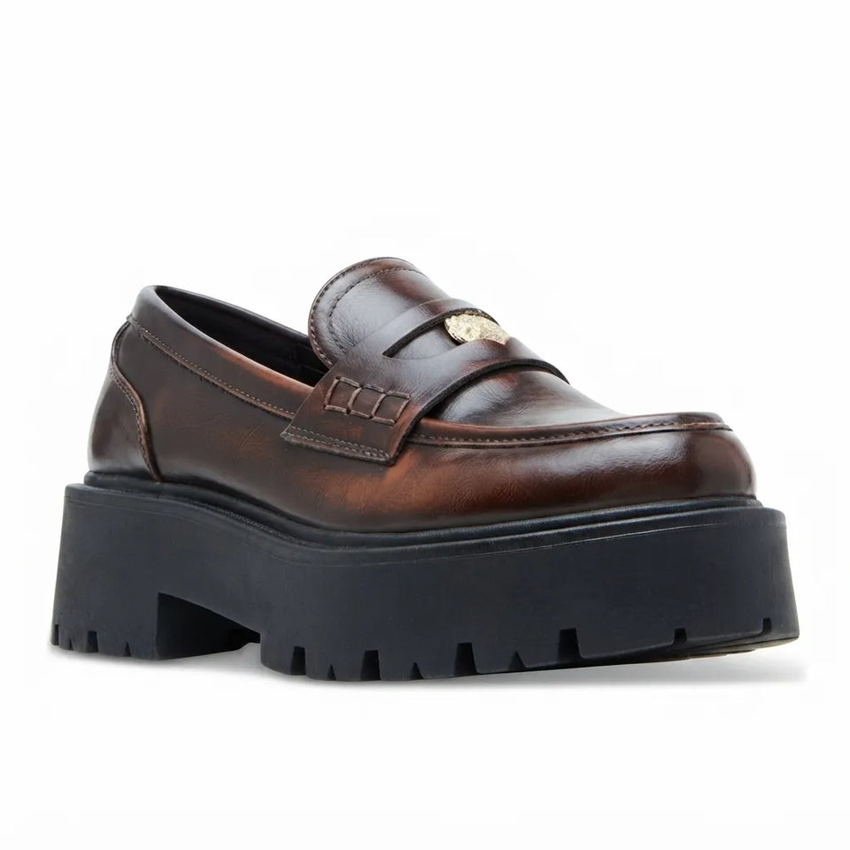 A dark brown leather penny loafer with a chunky black platform sole and a small gold-tone metal emblem on the strap, shown against a plain white background.