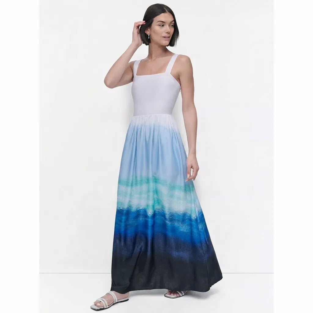 A woman modeling a sleeveless maxi dress with a white bodice and a blue ombre gradient skirt, standing against a plain white studio background.