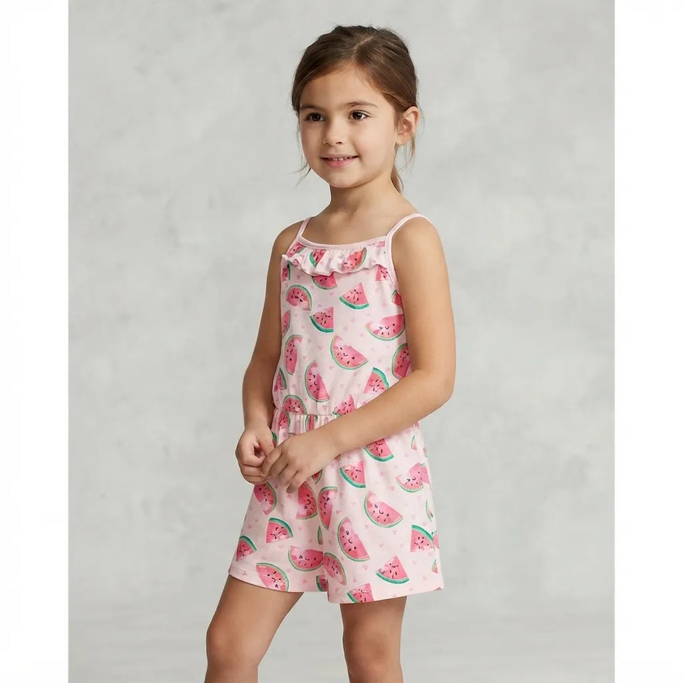 A young girl modeling a light pink sleeveless romper with a watermelon print, set against a neutral gray studio background.