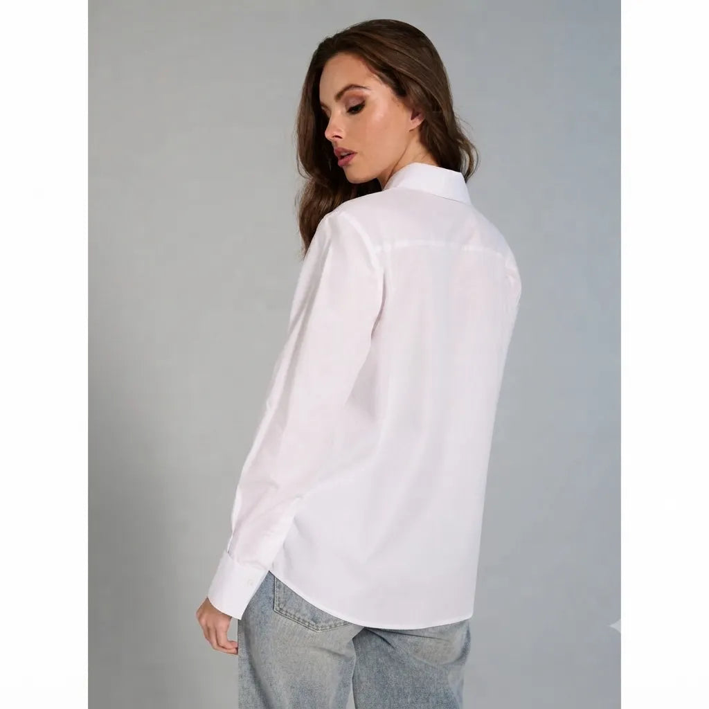 A woman wearing a white long-sleeve button-up shirt and light blue jeans, photographed from the back against a plain gray studio background.