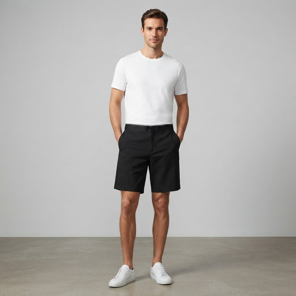 A man stands in a studio wearing a plain white short-sleeve crew-neck t-shirt, black shorts, and white sneakers against a light gray background.
