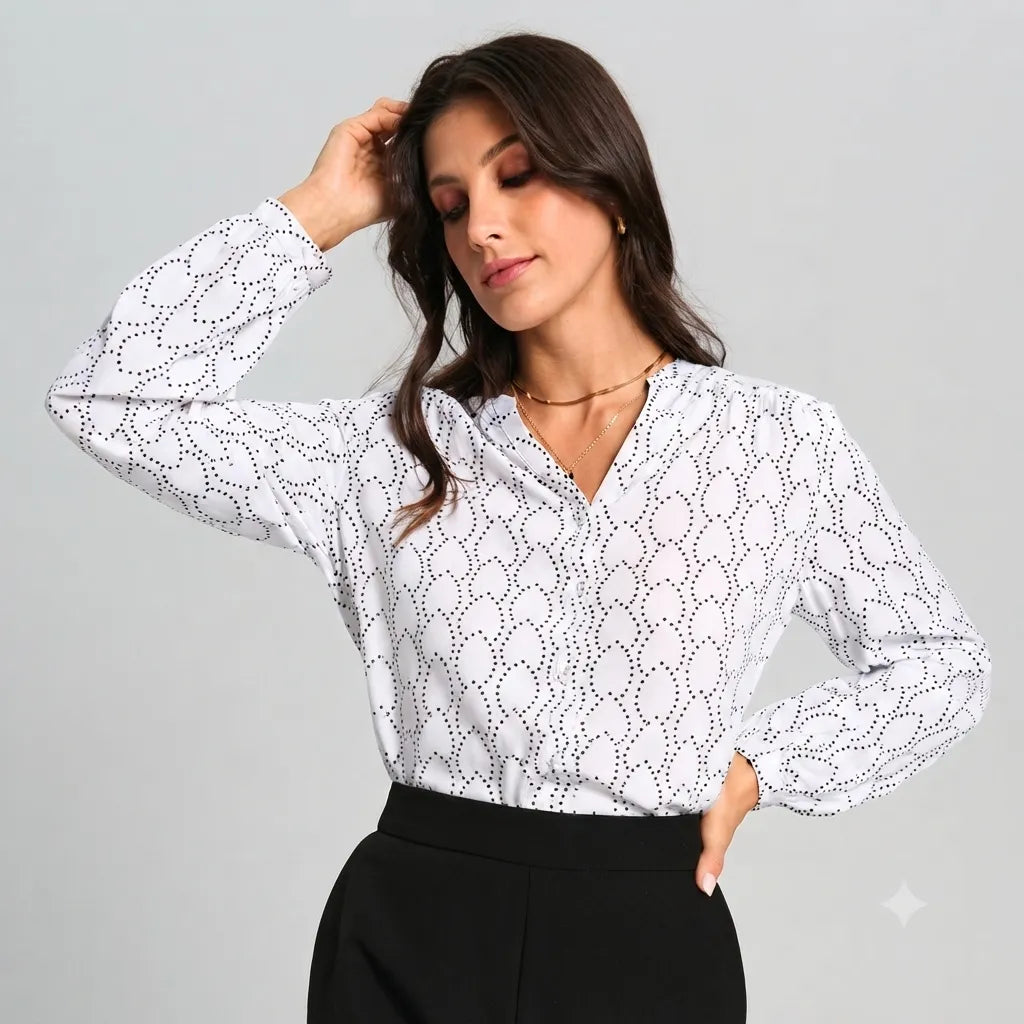A woman modeling a white long-sleeve blouse with a black dotted geometric pattern, paired with black pants, against a solid light gray studio background.