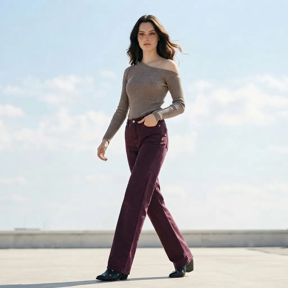 A woman walking outdoors on a sunny day, wearing a taupe off-the-shoulder knit sweater and dark burgundy wide-leg trousers with black shoes.