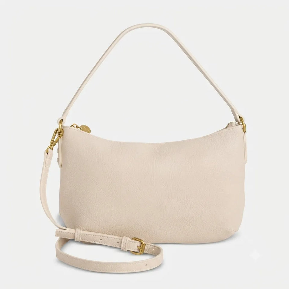 A light beige leather crescent-shaped shoulder bag with a matching adjustable strap and gold-tone hardware, shown on a clean off-white background.