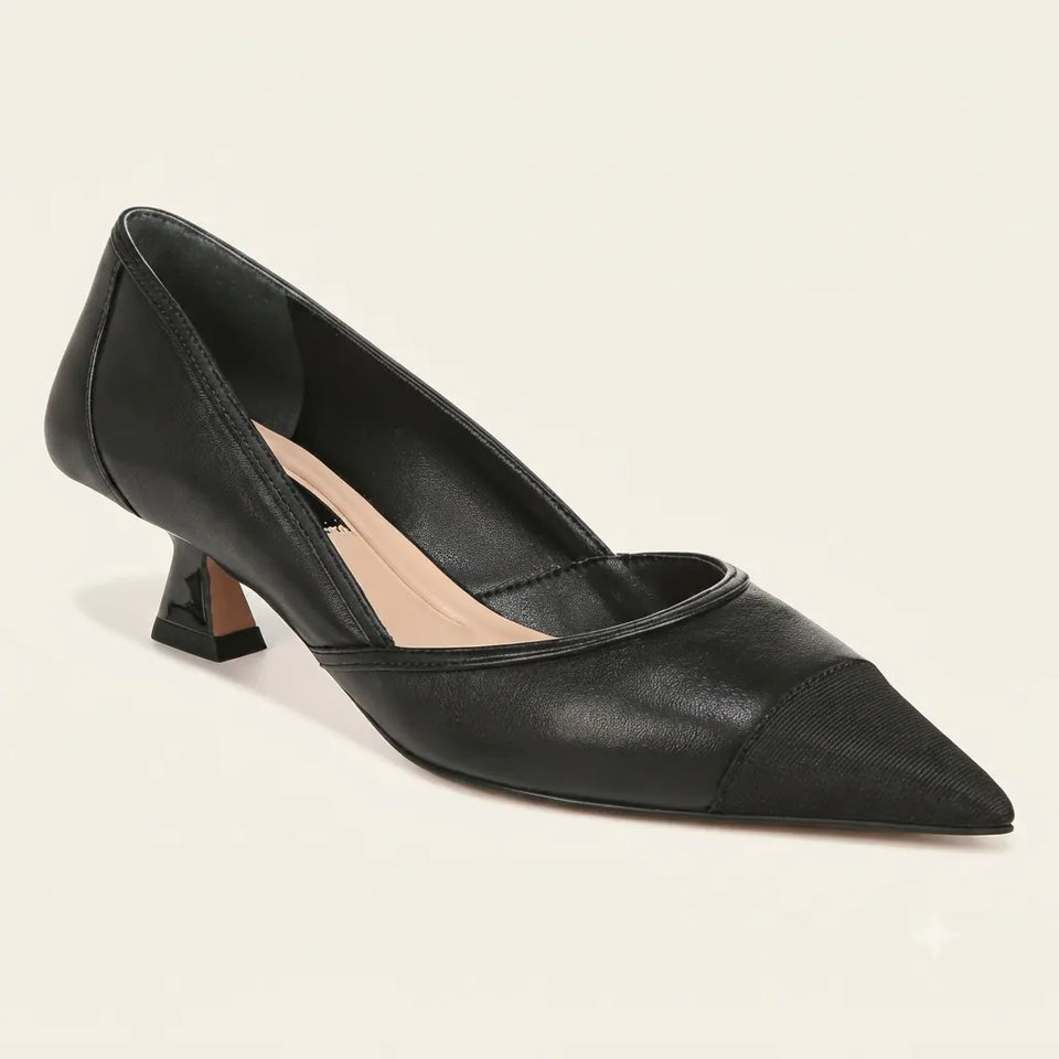 A black pointed-toe kitten heel pump with a cap toe and a light beige insole, shown from a three-quarters angle on a light cream background.