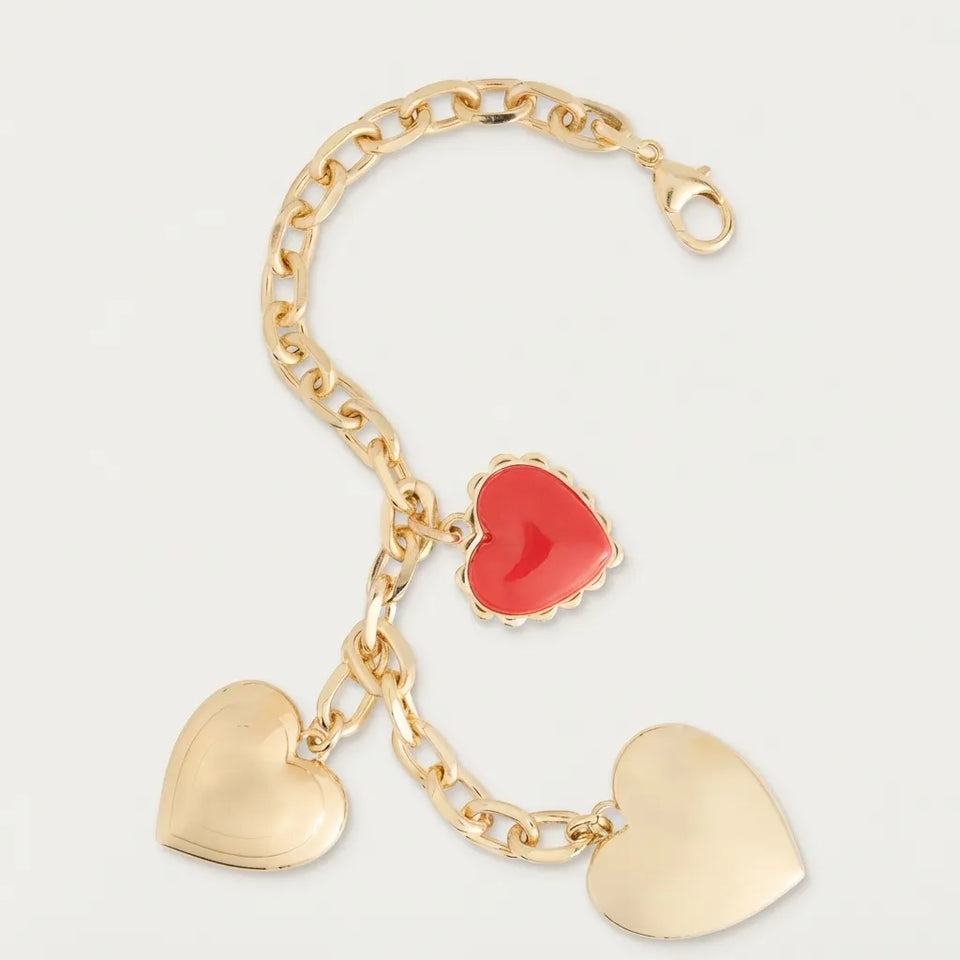 A gold-tone heart charm bracelet featuring three heart charms: two polished gold heart pendants and one smaller red heart charm, displayed on a light gray background.