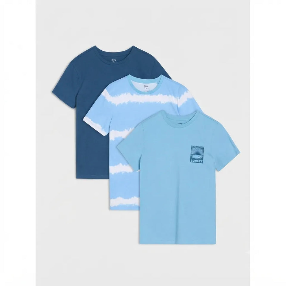 Three children's short-sleeve T-shirts in blue tones arranged in a stack on a light gray background. The back shirt is dark navy blue, the middle shirt is light blue and white tie-dye, and the front shirt is light blue with a small chest graphic.