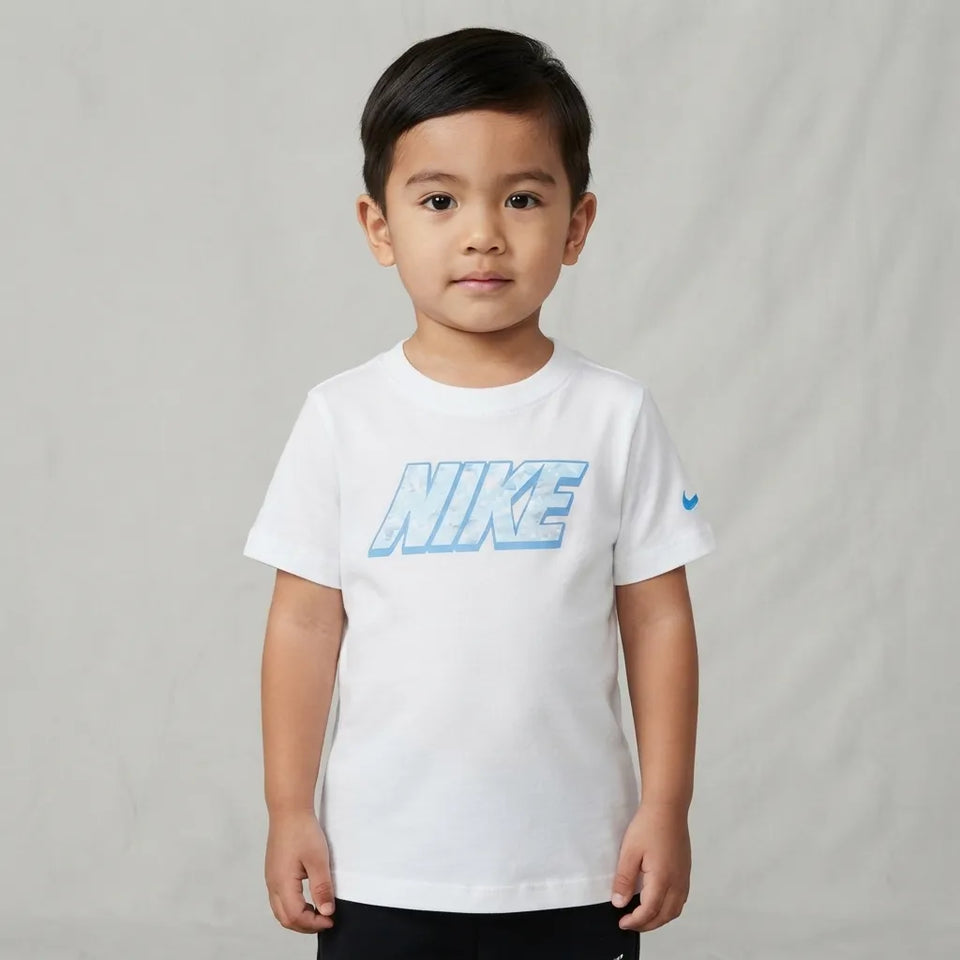 A young boy wearing a white Nike crewneck t-shirt with a light blue gradient logo on the chest and a small blue swoosh on the sleeve, standing against a light gray textured backdrop.