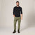 A man modeling olive green cargo pants with a black long-sleeve shirt and dark hiking boots, standing against a neutral light gray studio background.