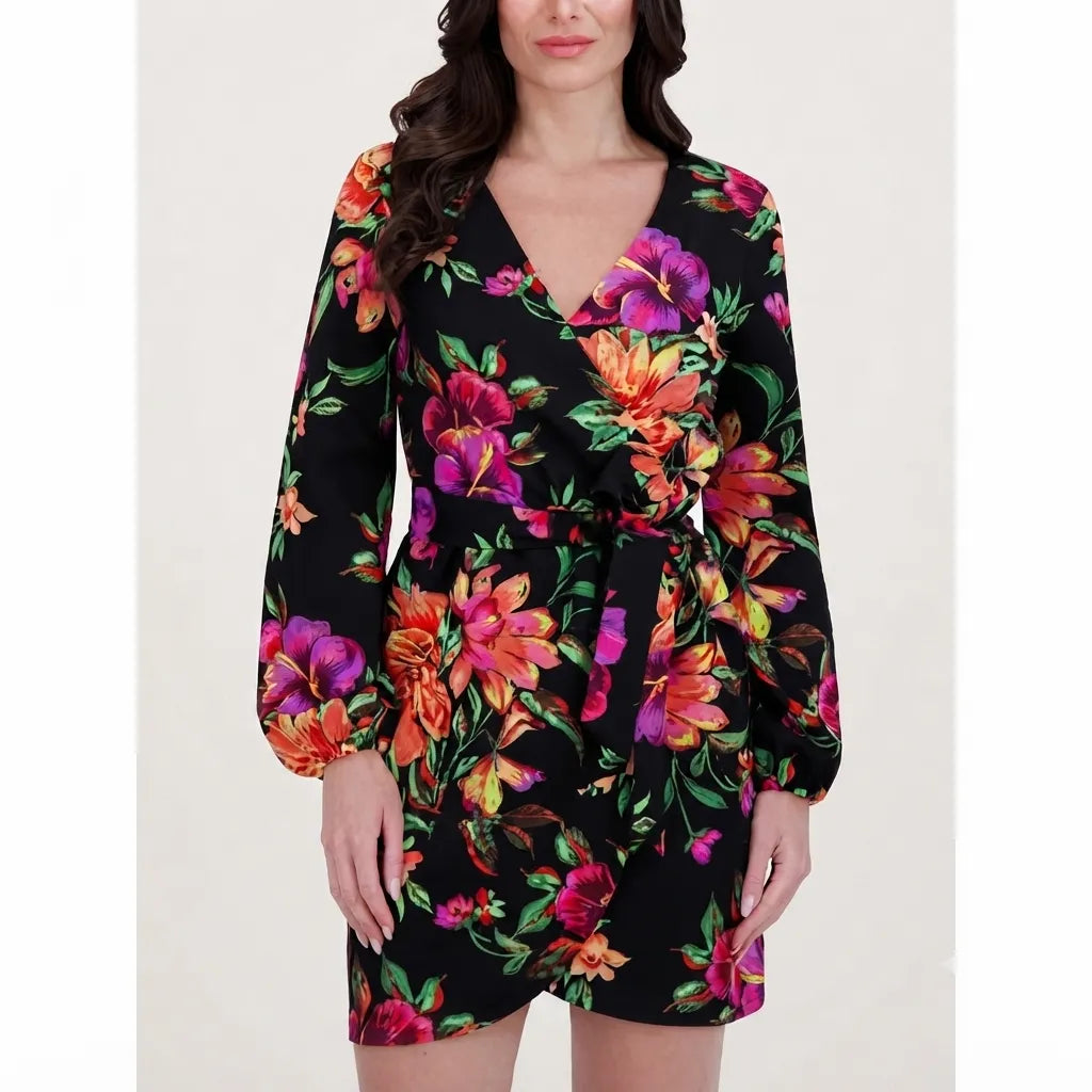 A woman wearing a long-sleeve black wrap dress with a vibrant multicolor floral print, featuring pink, orange, and purple flowers with green leaves.