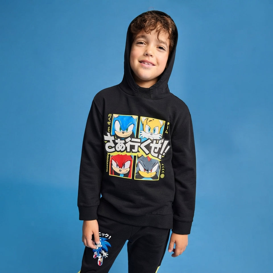 A young boy wearing a black Sonic the Hedgehog graphic hoodie and matching black pants, standing against a solid blue studio background.