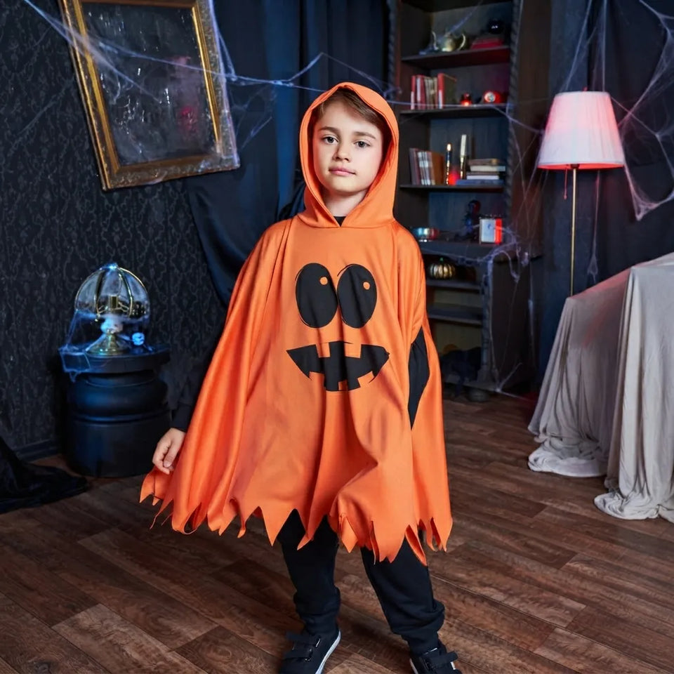 A child wearing an orange Halloween ghost costume with a black jack-o'-lantern face and jagged hem, standing in a dark, spooky room with cobwebs and a lamp.