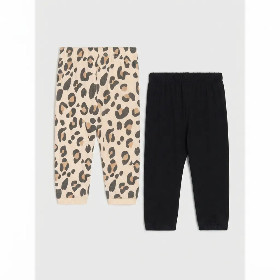 Two pairs of children's jogger pants laid flat on a light gray background: one pair is beige with a black and brown leopard print, and the other pair is solid black.