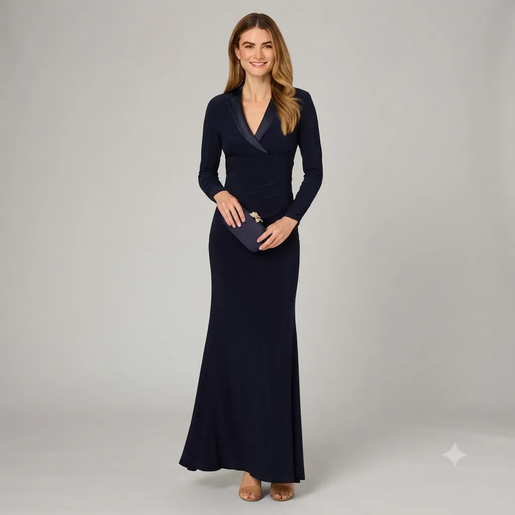 A woman modeling a long-sleeve navy maxi dress with a wrap-style V-neckline, holding a matching navy clutch against a light gray studio background.