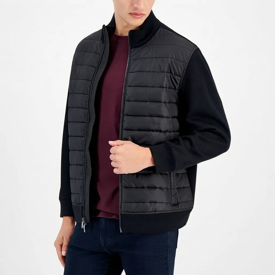 A man wearing a black puffer vest with black sleeves and a dark burgundy t-shirt underneath, paired with dark blue jeans, against a plain white background.