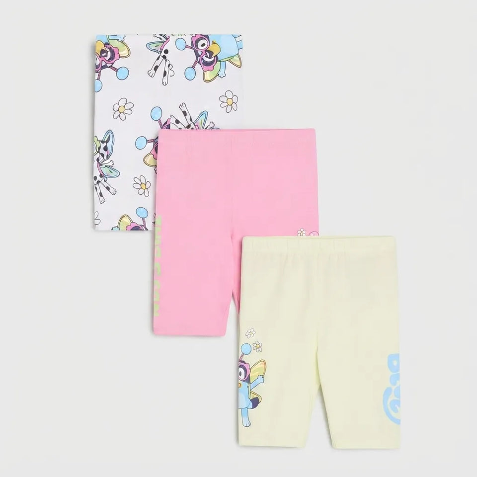 Three pairs of children's leggings or tights laid flat on a light gray background: one white pair with a colorful cartoon animal print, one solid pink pair, and one pale yellow pair with a small cartoon print near the hem.
