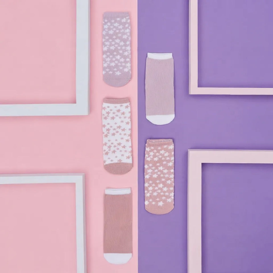 Five pairs of ankle socks arranged vertically on a split pink and purple background with decorative white frame borders. The socks feature pastel floral and star patterns in pink, lavender, and beige tones.