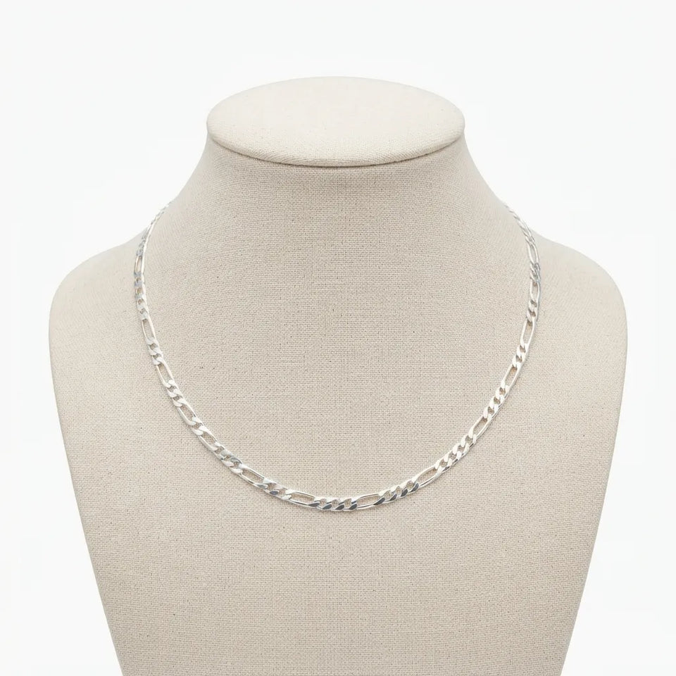 A silver Figaro chain necklace displayed on a beige fabric jewelry bust against a plain white background.