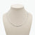 A silver Figaro chain necklace displayed on a beige fabric jewelry bust against a plain white background.