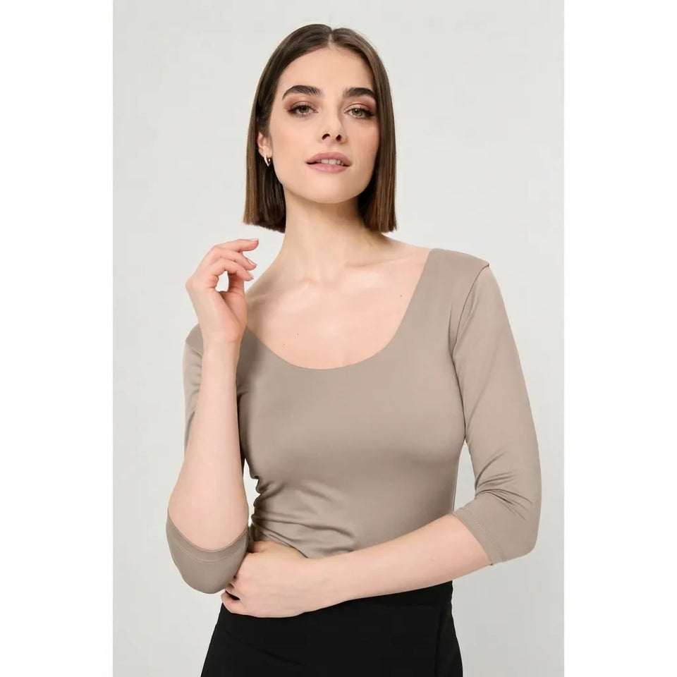 A woman modeling a fitted, scoop-neck three-quarter sleeve top in a taupe-beige color, paired with black bottoms, against a light gray studio background.