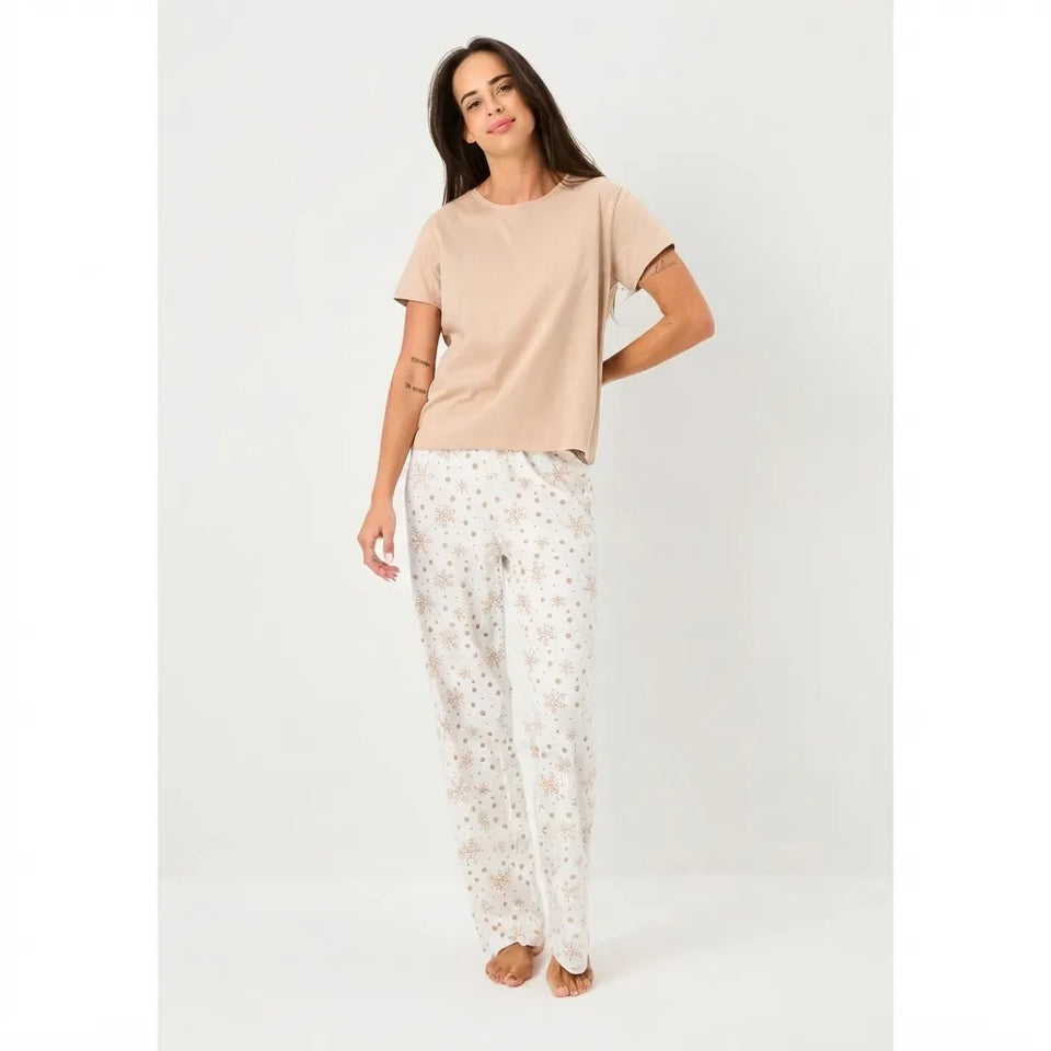 A woman modeling a two-piece pajama set consisting of a short-sleeve beige t-shirt and white pants with a small floral pattern, set against a plain light gray studio background.