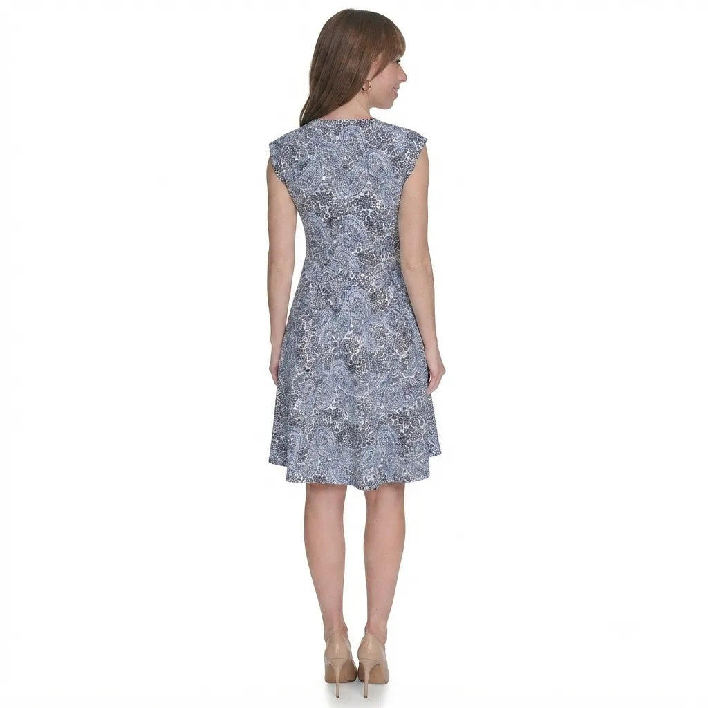 A woman viewed from the back wearing a sleeveless fit-and-flare dress with a blue and white abstract floral pattern, paired with beige high heels, against a plain white background.