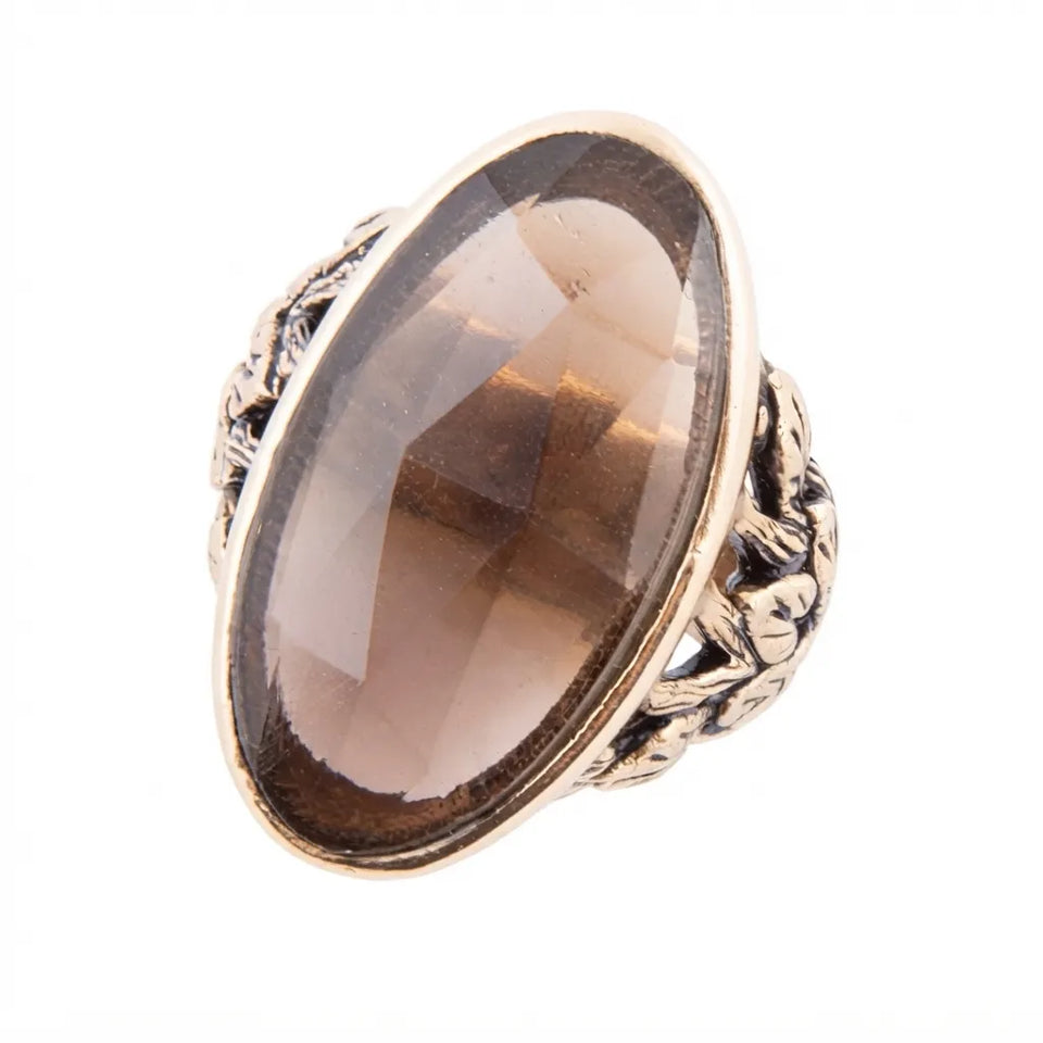 An oval smoky brown glass stone ring set in an antique gold-toned metal band with ornate floral detailing, shown on a plain white background.