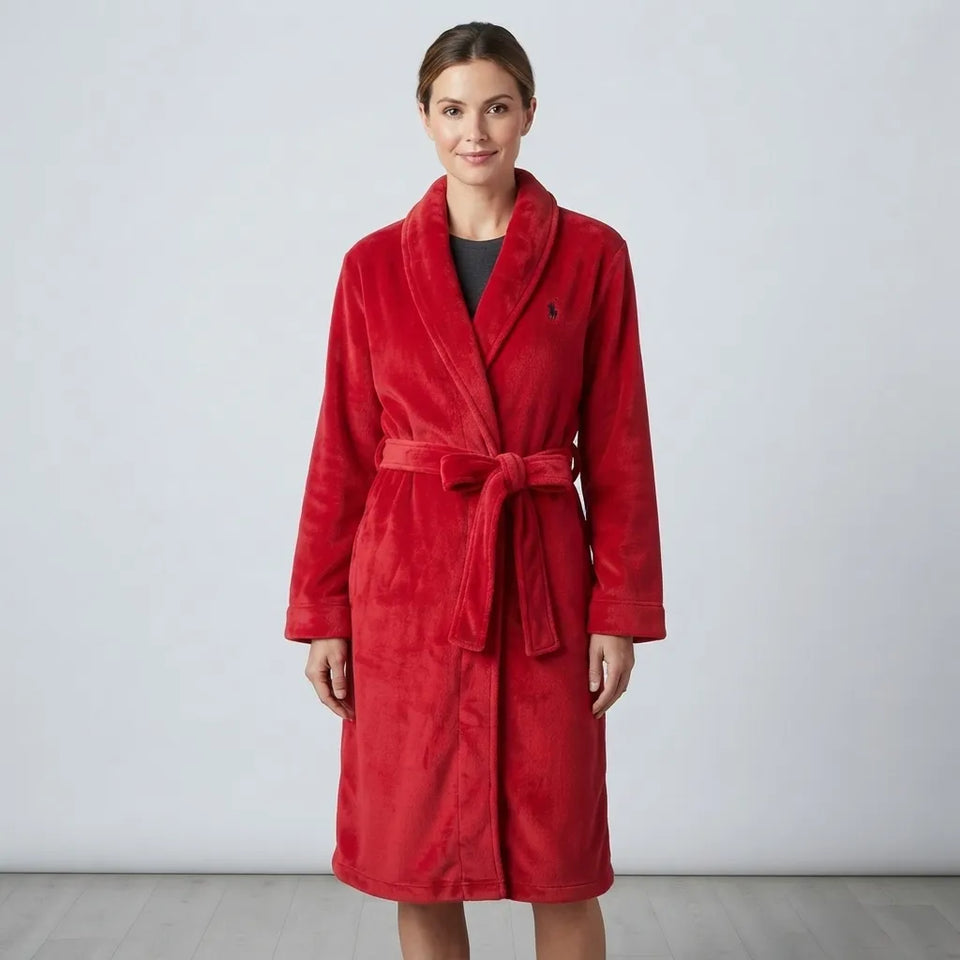 A woman wearing a plush red bathrobe with a tie belt, standing against a light gray studio background.