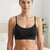 A woman modeling a black seamless bralette with thin straps and a wide underband, shown from the chest up in a softly lit indoor setting.