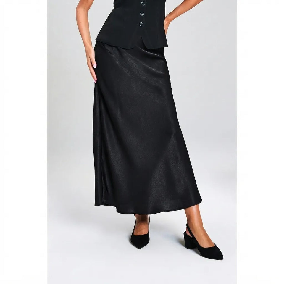 A model wearing a black satin midi skirt with a subtle sheen, paired with a black buttoned top and black pointed-toe slingback heels, set against a light gray studio background.