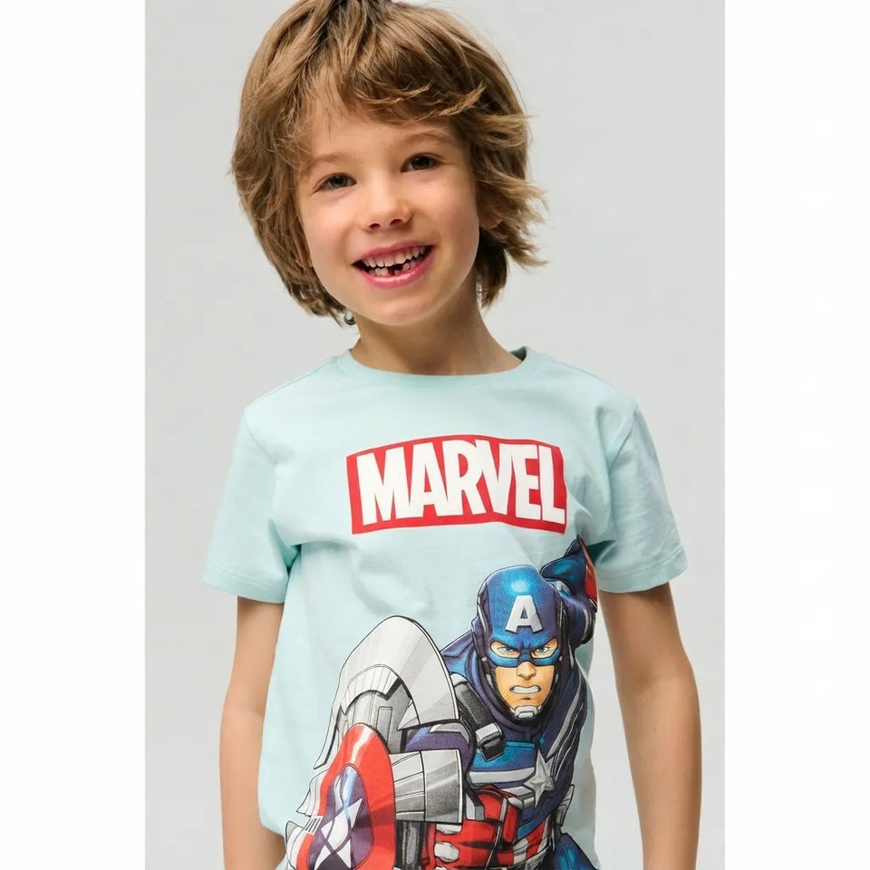 A smiling young boy wearing a light blue Marvel t-shirt with Captain America printed on the front, set against a plain light gray studio background.