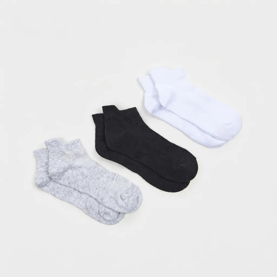 Three pairs of low-cut ankle socks laid flat on a light gray background: one pair is light gray heather, one pair is solid black, and one pair is solid white.