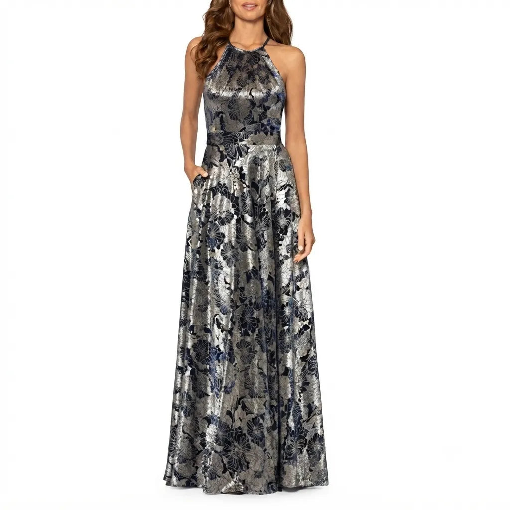 A sleeveless halter-neck floor-length gown with a metallic silver base and a dark navy floral pattern, shown on a model against a plain white background.