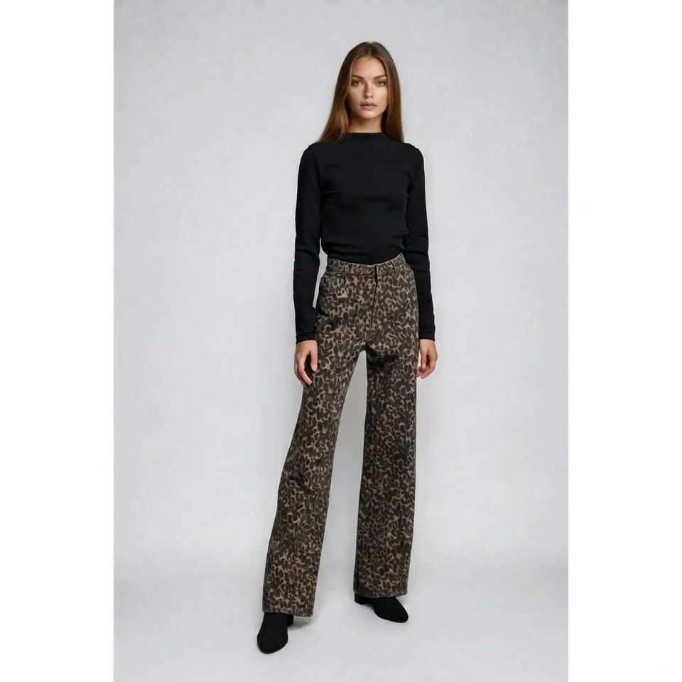 A woman modeling a black long-sleeve mock neck top and brown leopard-print wide-leg trousers against a light gray studio background.