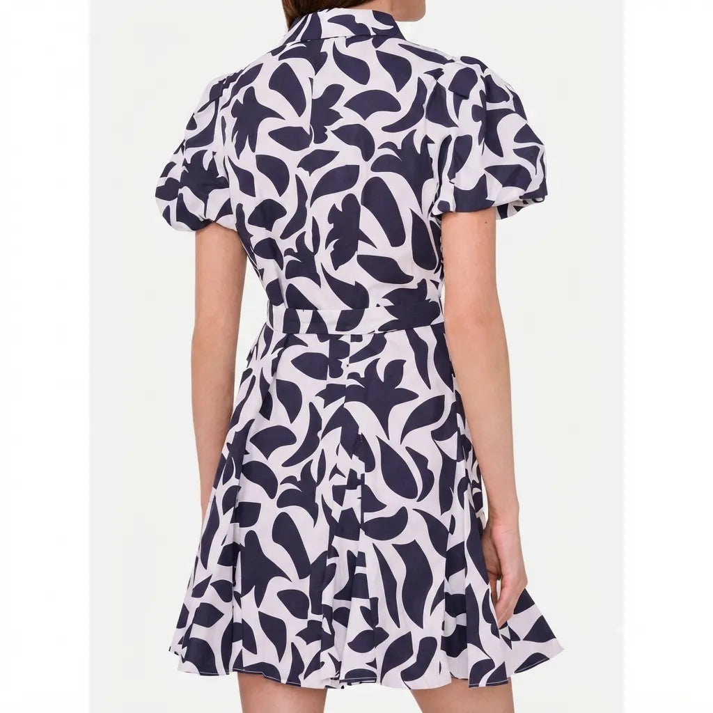 A woman wearing a short-sleeve collared dress with a bold abstract navy and off-white pattern, shown from the back against a light gray studio background.