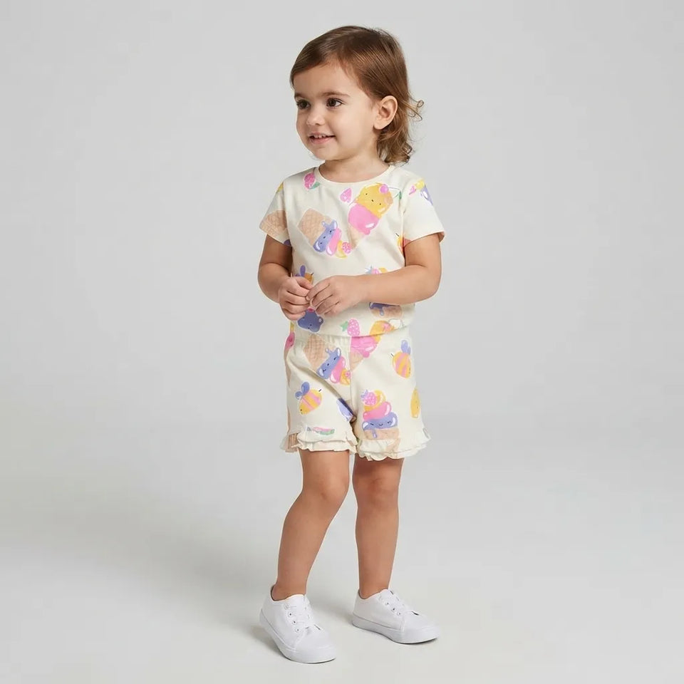 A toddler girl wearing a matching short-sleeve t-shirt and shorts set with a pastel mermaid print, standing against a light gray studio background.