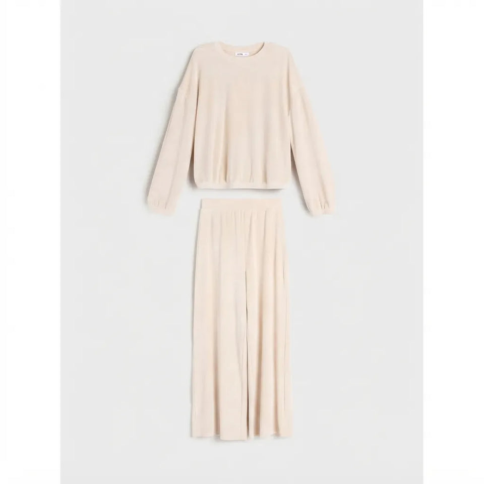 A two-piece knit loungewear set in a light cream-beige color, featuring a long-sleeve cropped top and matching wide-leg trousers, displayed on a neutral light gray background.