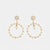 A pair of gold-toned statement dangle earrings featuring starburst studs, small pearl-like beads, and circular hoops accented with tiny clear stones, shown on a light gray background.