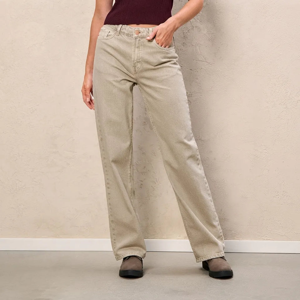 A person wearing light beige wide-leg jeans with a dark burgundy top and black flats, standing against a textured beige wall.
