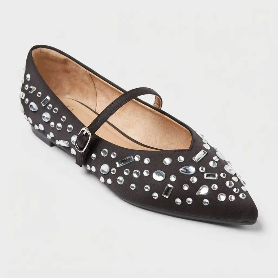 A single black pointed-toe flat shoe decorated with silver rhinestones and a small buckle detail on the strap, shown against a light gray background.
