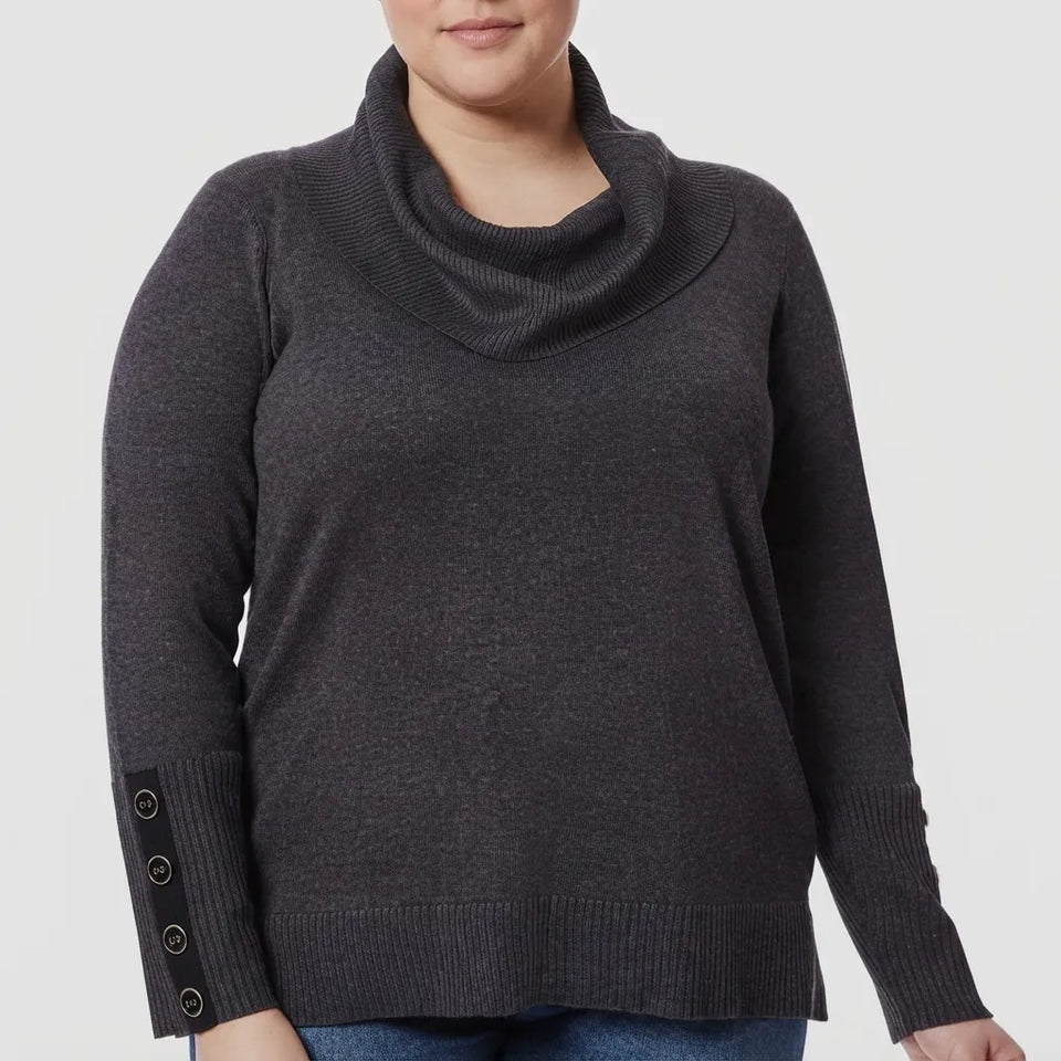 A woman wearing a dark charcoal gray cowl neck sweater with decorative buttons on the cuffs, shown from the chin down against a light gray background.